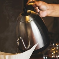 person pouring water from stainless steel kettle