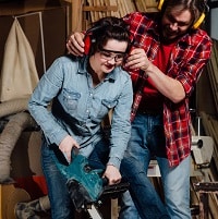 Carpenter woman and man with electric chainsaw in workshop